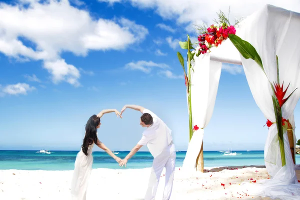 Любящая пара в день свадьбы на тропическом пляже возле бамбуковой арки — стоковое фото