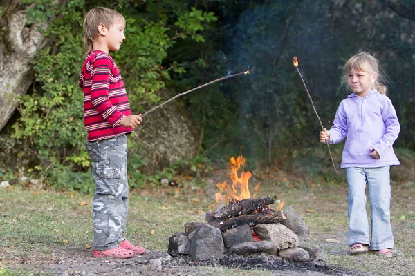 To barn, gutt og jente, som lekte med ild på en naturlig bakken- – stockfoto