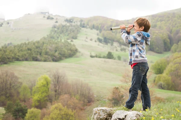 Unga barn pojke tittar genom kikaren till sidan land — Stockfoto