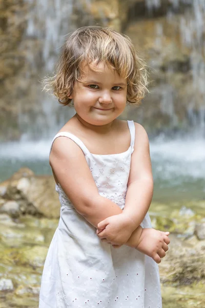 Mignon souriant tout-petit enfant fille sur fond de cascade — Photo