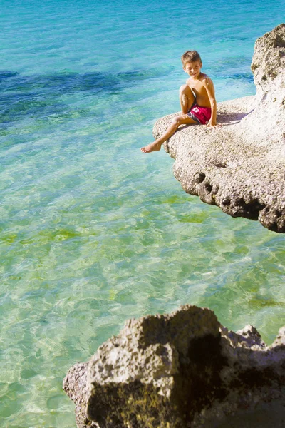 Young child boy sitting on rocks on tropical sea background — Stock Photo, Image