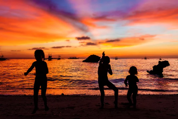 Três crianças silhuetas no pôr do sol fundo do mar — Fotografia de Stock