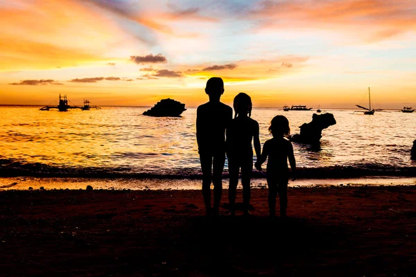 Três crianças silhuetas no pôr do sol fundo do mar — Fotografia de Stock