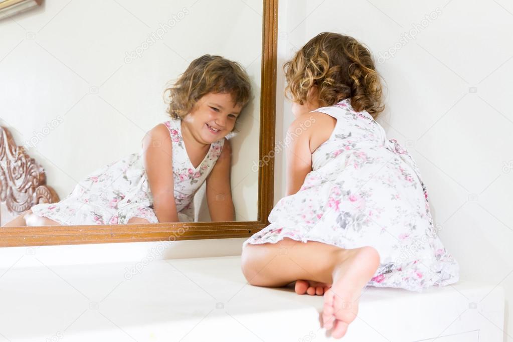 young beautiful child girl looking at herself in mirror at home