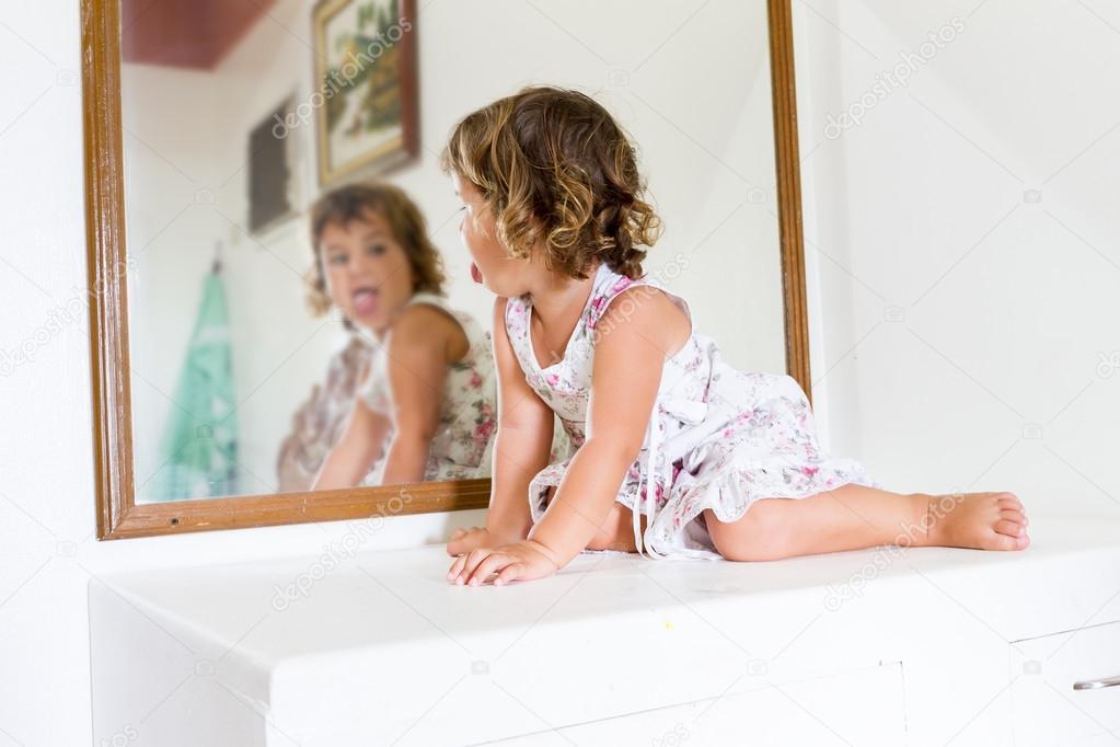 young beautiful child girl looking at herself in mirror at home