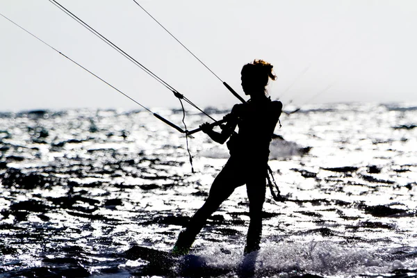 Uma jovem kite-surfista cavalga contra o sol — Fotografia de Stock