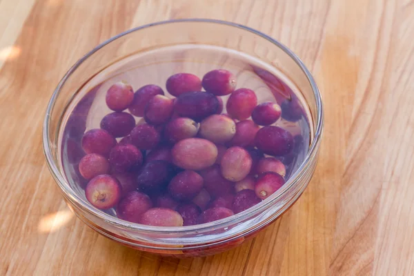 Red grapes in water served in glass bowl on wooden cutting board — Stock Photo, Image