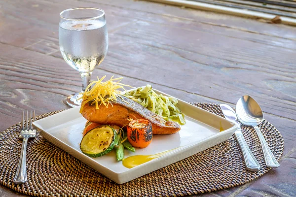 Grilled salmon steak served with pasta and vegetables in a small — Stock Photo, Image