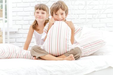Beyaz yatakta evde oynayan iki küçük mutlu çocuklar