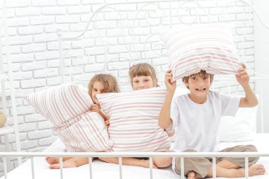 Beyaz yatakta evde oynayan üç küçük mutlu çocuklar
