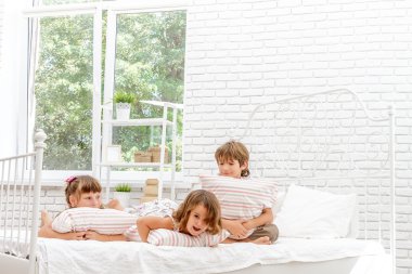Beyaz yatakta evde oynayan üç küçük mutlu çocuklar