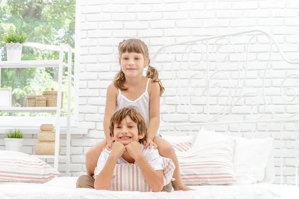 Dos pequeños niños felices jugando en la cama blanca en casa — Foto de Stock