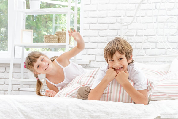two little happy kids playing on white bed at home