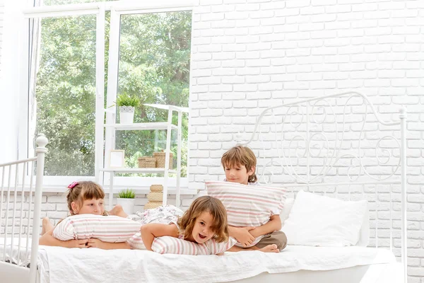 Beyaz yatakta evde oynayan üç küçük mutlu çocuklar