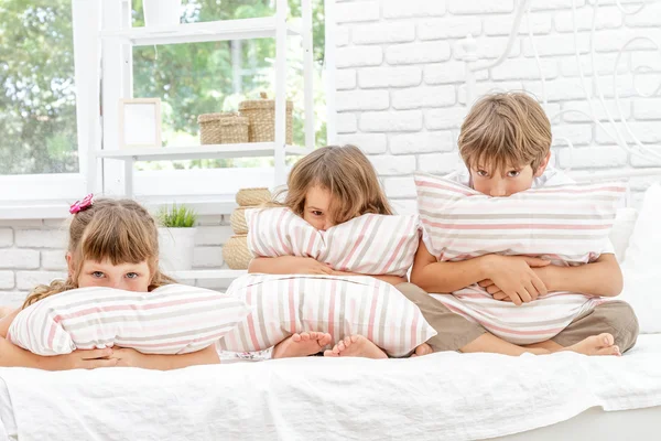 Tři malé šťastné děti hrají na bílé posteli doma — Stock fotografie