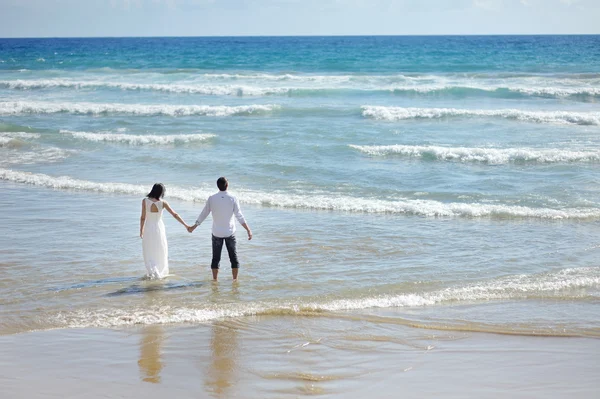 Bride and groom walking on the beach in sunny day — Stock Photo, Image