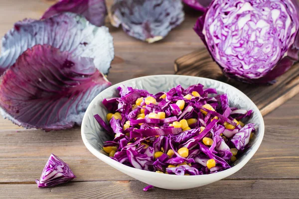 Red cabbage salad with corn grains in a plate on a wooden table. Vegetarian food