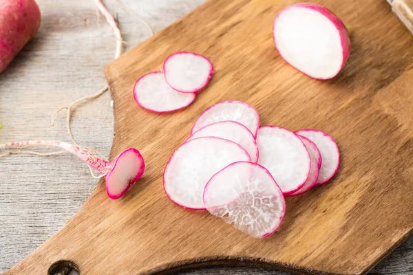 Fresh sliced radish on a cutting board on a wooden table. Vegetables for a vegetarian diet. Rustic style. Top view