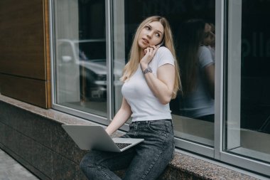 Fazladan para kazanmak, ek iş yapmak, para kazanmak, hobileri paraya çevirmek, iş ekonomisi, dijital göçebe. Genç bir kadın, laptopu ve akıllı telefonu olan bir öğrenci dışarıda çalışıyor.