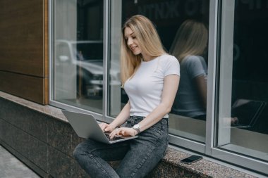 Fazladan para kazanmak, ek iş yapmak, para kazanmak, hobileri paraya çevirmek, iş ekonomisi, dijital göçebe. Genç bir kadın, laptopu ve akıllı telefonu olan bir öğrenci dışarıda çalışıyor.