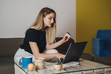 Çevrimiçi alışveriş, Kara Cuma indirimi, Holiday e-ticaret, internet bankacılığı, harcama para konsepti. Evde elinde kredi kartı olan, dizüstü bilgisayar ve cep telefonu kullanan genç bir kadın.