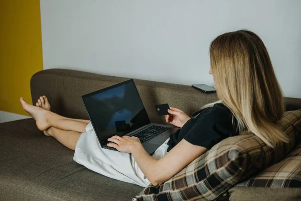 Compra de impulso, compras en línea, moda rápida, adicto a las compras, el gasto de concepto de dinero. Mujer joven en casa con tarjeta de crédito y el uso de ordenador portátil y teléfono celular — Foto de Stock