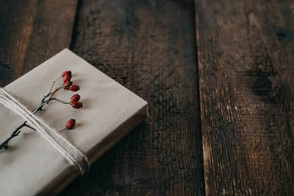 Eco-Friendly, Sustainable, zero waste christmas gift wrapped in kraft paper with twine and berry decor. Christmas wrapped gift box with natural decor on wooden background