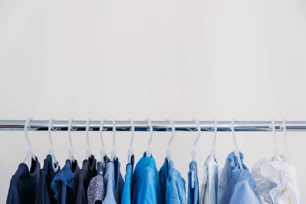Fast fashion, Sustainable fashion, minimalist wardrobe. Variety of female blue clothing on hanging on white background with copy space. Fashion minimal style banner