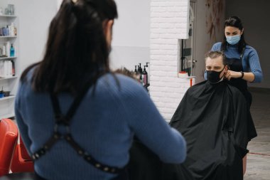 Berber dükkanları, kuaförlerin kapanması, ikinci tecrit. Kuaför maskesiyle kuaför kuaförde erkek müşteriyi soyuyor ve tarıyor. Kuaför ve erkek müşteri koruyucu yüz maskeleri takıyor..