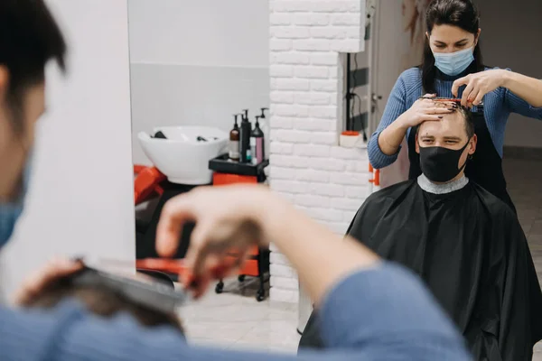 Barber shops, hair salons shutting down, second lockdown. Hairdresser in face mask peeling and combing male client in hair salon. Hairdresser and man client are wearing protective face masks.