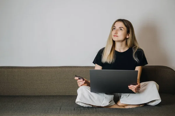 Compra de impulso, compras en línea, moda rápida, adicto a las compras, el gasto de concepto de dinero. Mujer joven en casa con tarjeta de crédito y el uso de ordenador portátil y teléfono celular — Foto de Stock