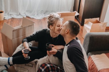 Taşınma günü, yeni ev, Sevgililer Günü, kutuları boşaltma, yeni evliler konsepti. Yeni eve taşınmayı kutlayan ve şarapla eğlenen çift.