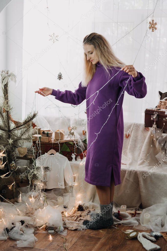 Holiday christmas decorating at home. Young woman putting ornaments on xmas tree, setting up lights. Budget hristmas Home Decor Ideas