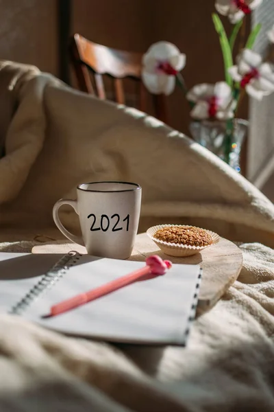 2021 цели, новый год резолюции, начать планирование. Чашка с текстом и открытый блокнот, ручка на кровати при солнечном свете. Кубок с рукописным текстом 2021 и блокнот готов к планированию — стоковое фото