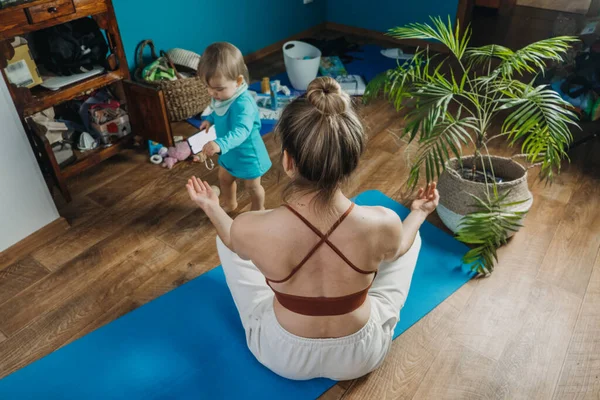 Junge Mutter sitzt auf dem Boden, genießt Meditation machen Yoga-Übungen zu Hause mit seiner kleinen Tochter Baby-Mädchen. Psychische Gesundheit, Selbstversorgung, Kein Stress, gesunde Gewohnheit, Beschwichtigung, Konzept zur Angstlinderung — Stockfoto