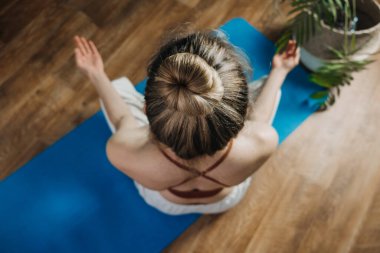 Yoga pozunda oturan genç kadın evde yoga yaparak meditasyonun tadını çıkarıyor. Zihinsel sağlık, kişisel bakım, stres yok, sağlıklı alışkanlık, farkındalık yaşam tarzı, endişe giderme konsepti