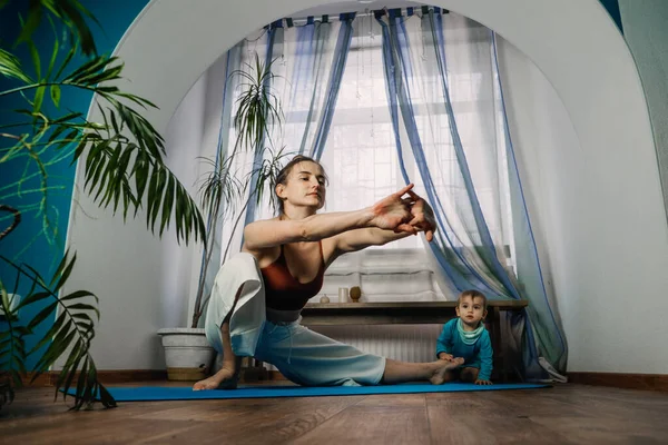 Home Fitness, Training im neuen Normalzustand, Pandemiezeit, Yoga zu Hause. Mutter trainiert, praktiziert Yoga mit Baby-Mädchen im selben Raum — Stockfoto