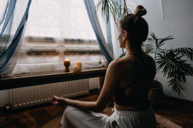 Öz-bakım, kendine şefkat, salgın sonrası dünyada zihinsel refah. Zihinsel sağlık, refah, endişeden kurtulmak için meditasyon. Yerde oturan genç kadın evde yoga ve meditasyon yapıyor.