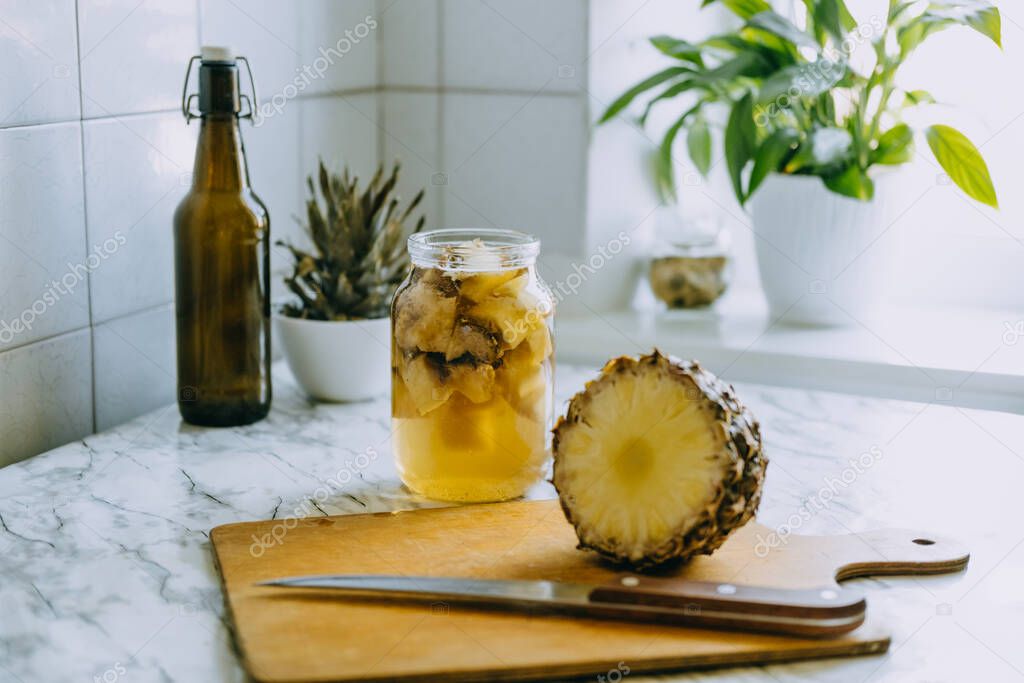 Fermented pineapple kombucha drink tepache. Cooking process of homemade probiotic superfood pineapple beverage. Drink jar and sliced pineapple on home kitchen