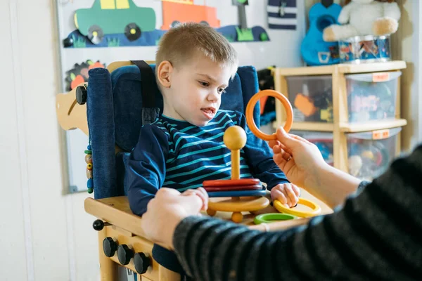 Engelli çocuklar için etkinlikler. Özel ihtiyaçları olan çocuklar için okul öncesi aktiviteler. Serebral felçli çocuk özel koltukta annemle evde oynuyor.. — Stok fotoğraf