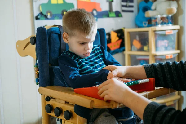 Aktiviteter för barn med funktionsnedsättningar. Förskoleverksamhet för barn med särskilda behov. Pojke med med Cerebral Palsy i särskild stol lek med mamma hemma. — Stockfoto