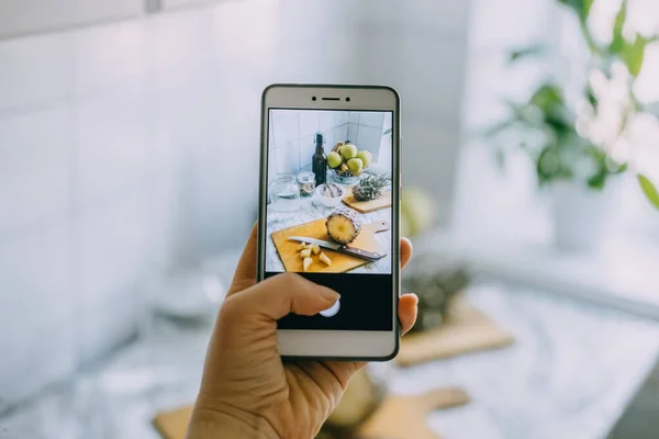 Food-Bloggerin fotografiert auf Smartphone für soziale Netzwerke. Weibliche Hand hält Handy mit Foto des Kochprozesses von hausgemachten fermentierten probiotischen Superfood-Ananasgetränk — Stockfoto