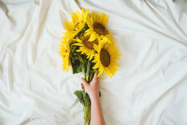 Candid auténtico ramo de girasoles amarillos sobre tela de fondo blanco. Fondo con ramo de girasoles amarillos sobre sábana blanca. Días soleados, concepto floral de verano — Foto de Stock