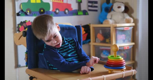 Sensorische activiteiten voor kinderen met een handicap. Voorschoolse activiteiten voor kinderen met speciale behoeften. Jongen met Cerebral Palsy in speciale stoel spelen en glimlachen thuis. — Stockvideo