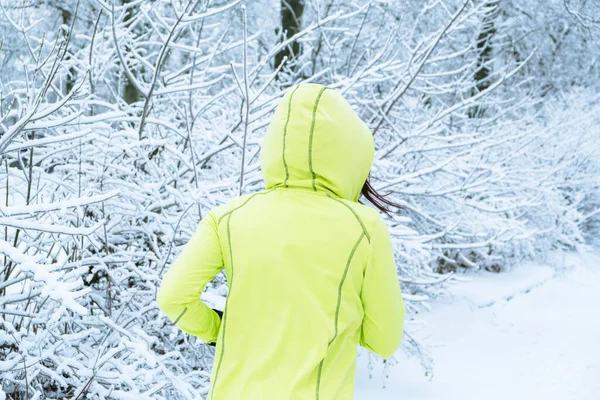 Middle aged woman in green sportswear running in winter snow park. Happy fit middle aged woman trail running in the snowy forest. Winter Sport, fitness inspiration and motivation.