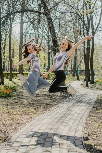 Gen z chicas disfrutando al aire libre, expresando emociones positivas. Foto al aire libre de dos amigas divirtiéndose en el parque. Dos jóvenes felices y alegres saltando y riendo juntas —  Fotos de Stock