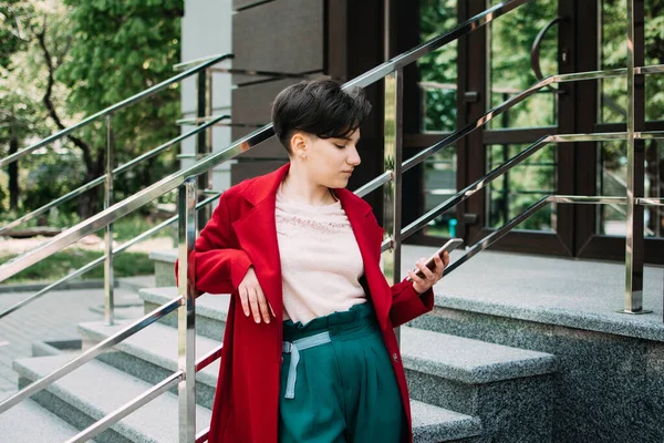 Gén z, médias sociaux, influenceur, technologie, concept des jeunes du millénaire. Jeune fille brune avec les cheveux courts en utilisant le téléphone mobile extérieur — Photo