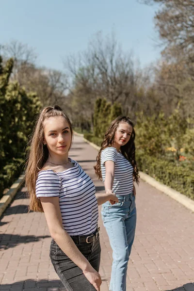 Gen z flickor njuter utomhus, uttrycker positiva känslor. Utomhus foto av två flickvänner som har roligt i parken. Två glada unga kvinnor hoppar och skrattar tillsammans — Stockfoto