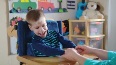 Engelli çocuklar için etkinlikler. Özel ihtiyaçları olan çocuklar için okul öncesi aktiviteler. Annem evdeki özel koltukta beyin felçli çocukla oynuyor.