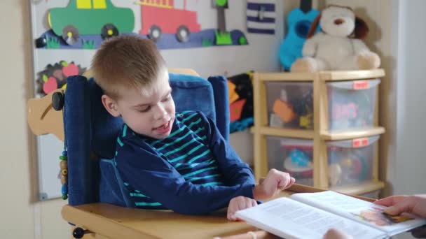 Activities for kids with disabilities. Preschool Activities for Children with Special Needs. Mom is reading book for Boy with Cerebral Palsy in special chair at home — Stock Video